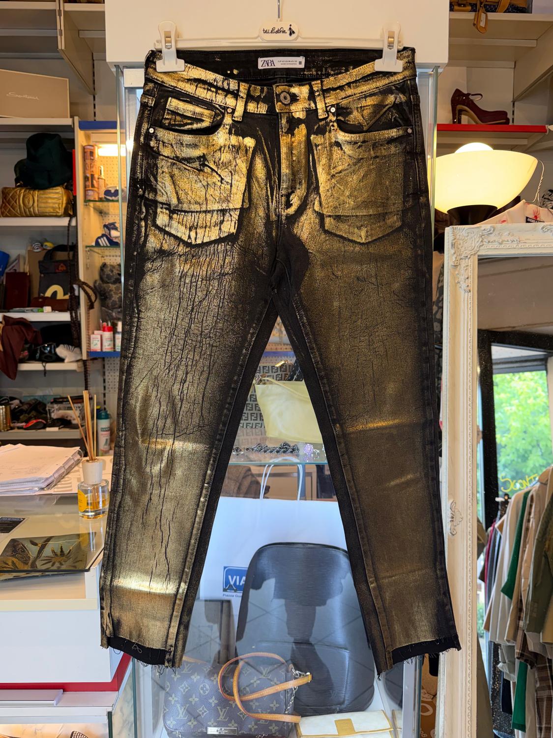 Gold trousers hanging in a shop, surrounded by handbags and clothes. Background with shelves and warm light.