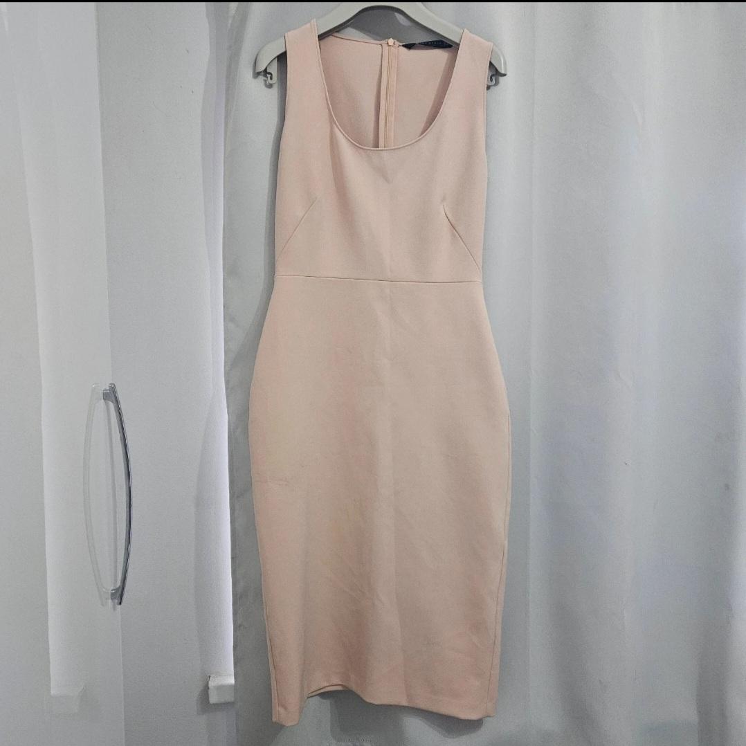Sleeveless beige dress hanging on a hanger against a background of white curtains.