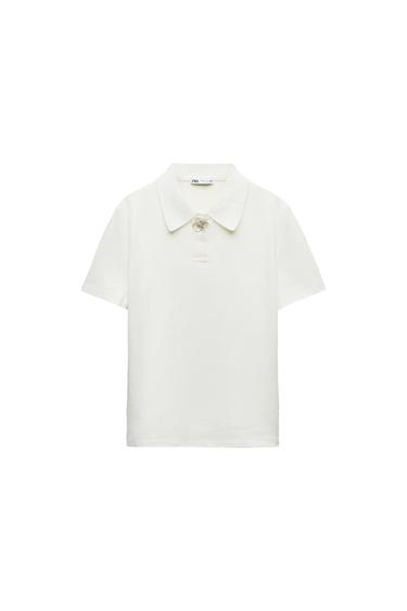 White short-sleeved polo shirt with a classic collar and decorative detail on the top button. Visible label inside the collar.