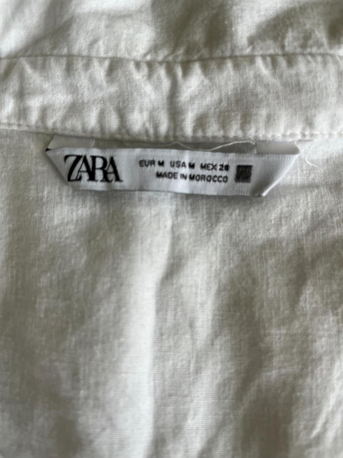 White clothing label with the text "ZARA, EUR M, USA M, MEX 28, MADE IN MOROCCO" on wrinkled fabric.