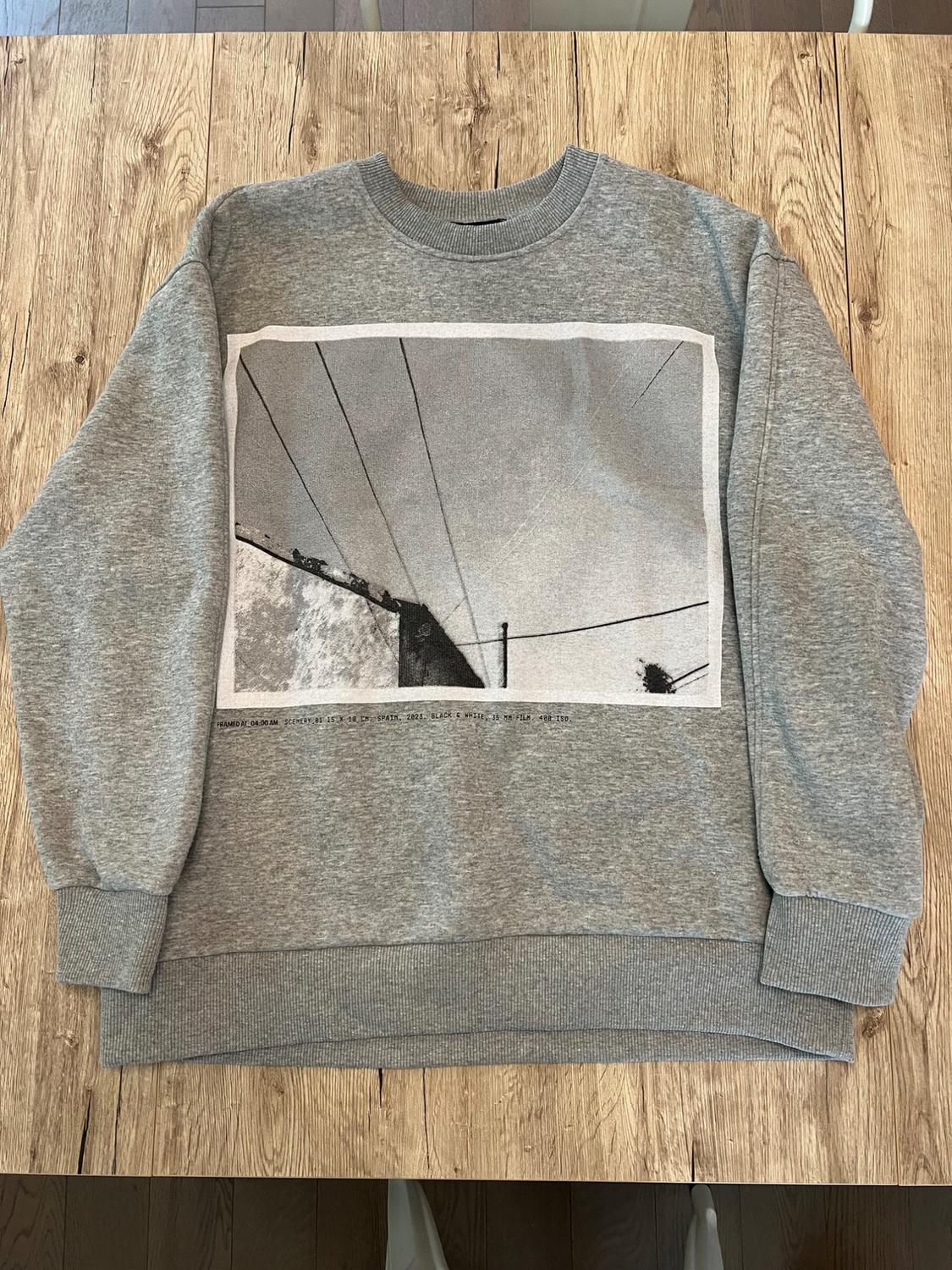 Grey sweatshirt on wood with photo and text: FRAMED AT 04:00 AM SCENERY 01 15 X 10 CM, SPAIN, 2023. BLACK & WHITE, 35 MM FILM, 400 ISO.