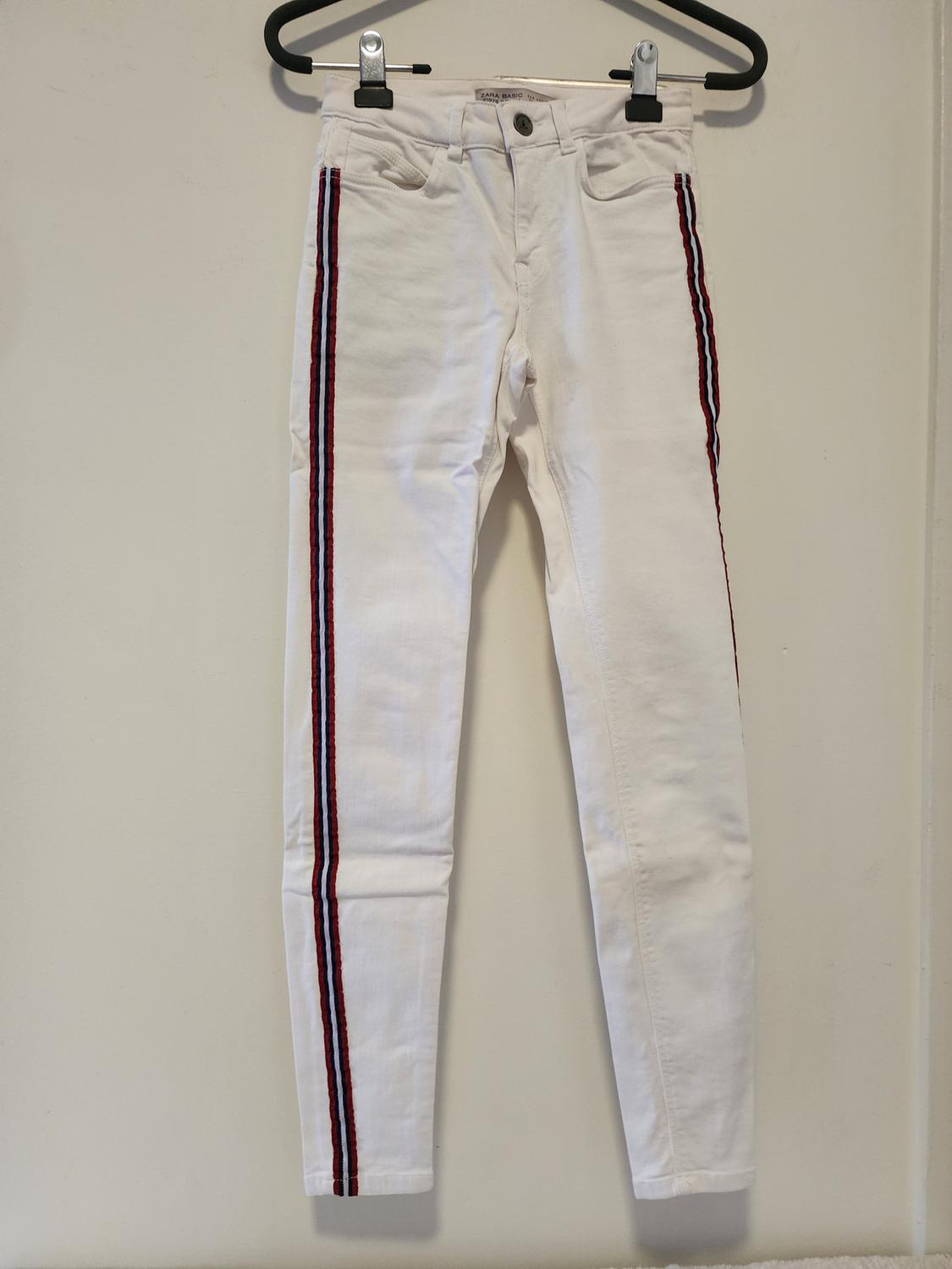 Front view of white pants with red and black side stripes, front pockets, and button closure.
