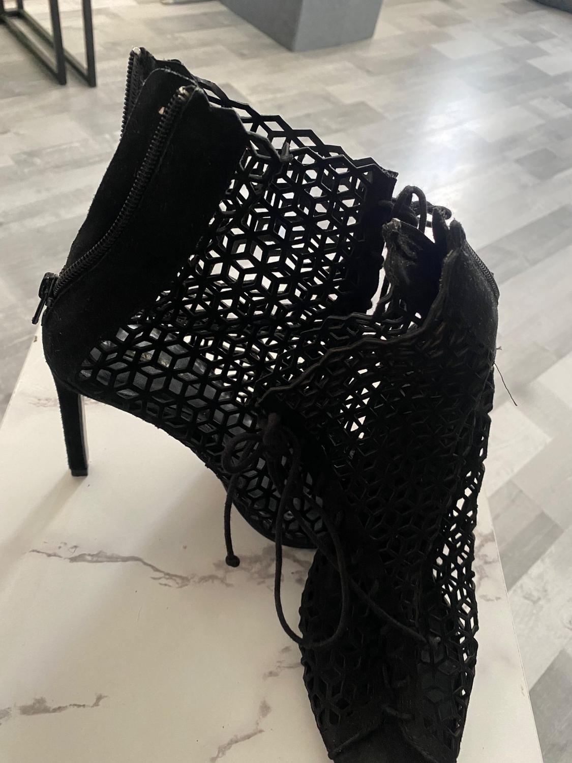 Detail of black ankle boot with geometric mesh design and side zip.
