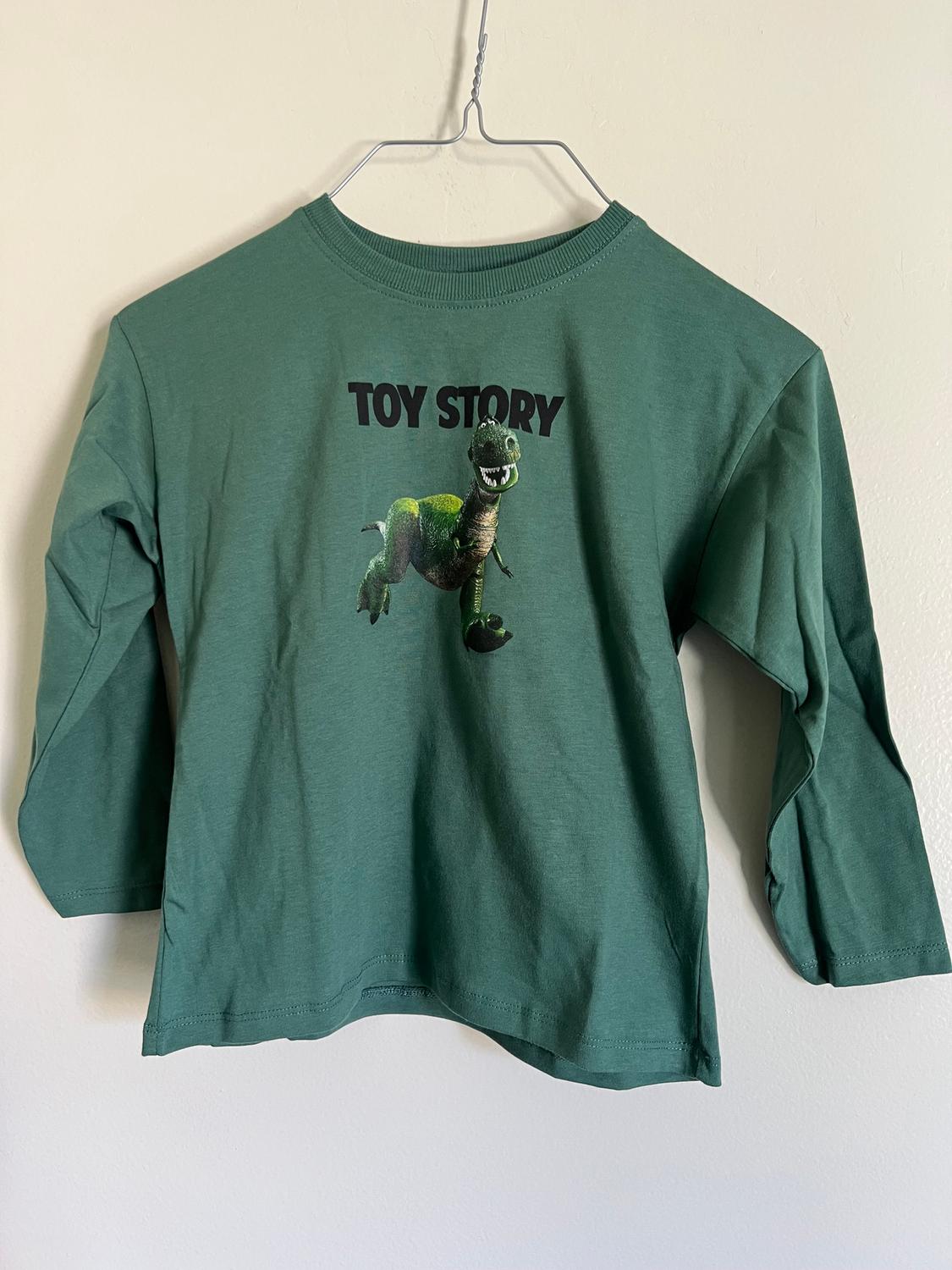 Green, long-sleeved T-shirt hanging on a hanger, with "TOY STORY" text and a green dinosaur print on the front.