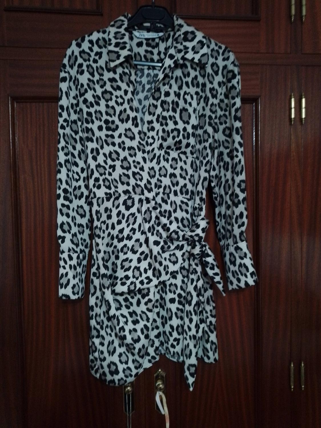 Black and white leopard print long-sleeved blouse, hanging on a hanger in front of a wooden wardrobe.