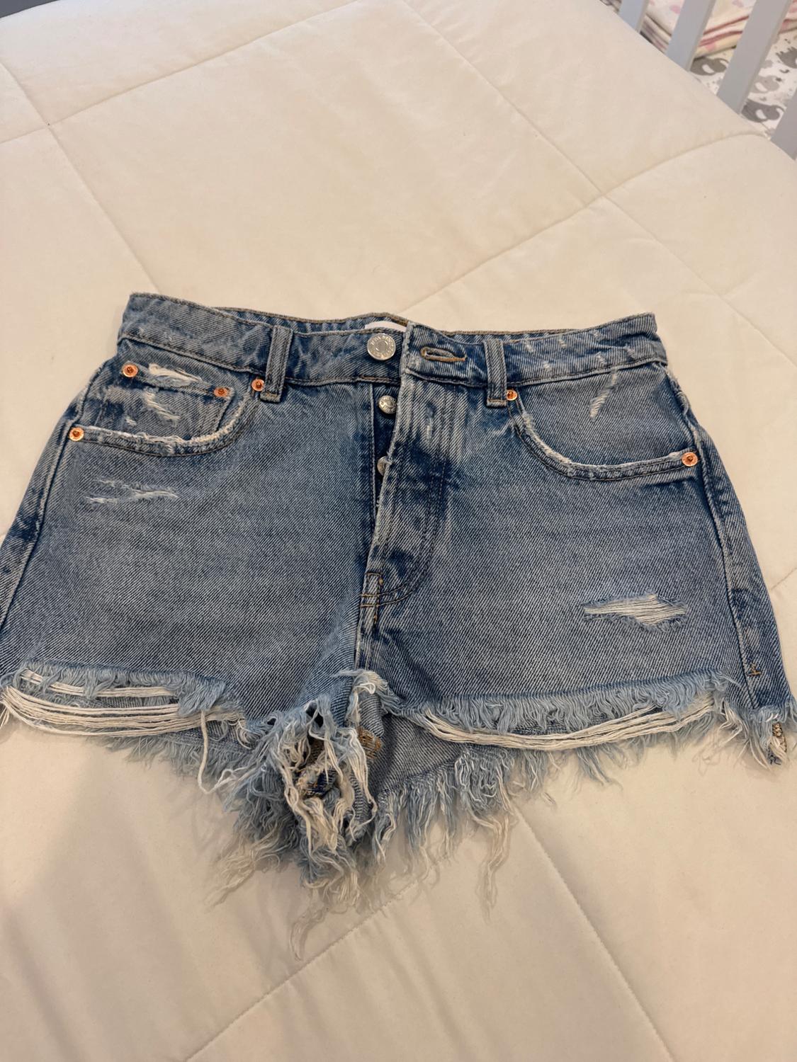 Distressed denim shorts with frayed hem and ripped details, on a white quilted bedspread.