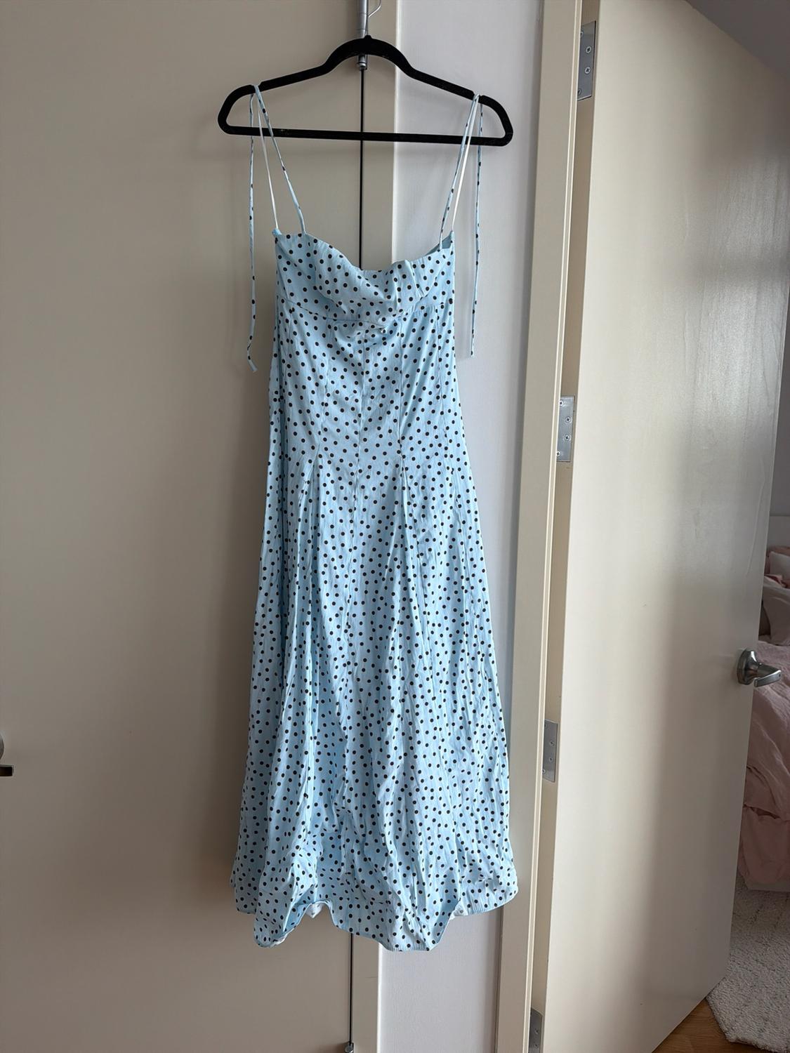 Light blue dress with black polka dots and thin straps hanging on a black hanger on an ajar white door in a room.