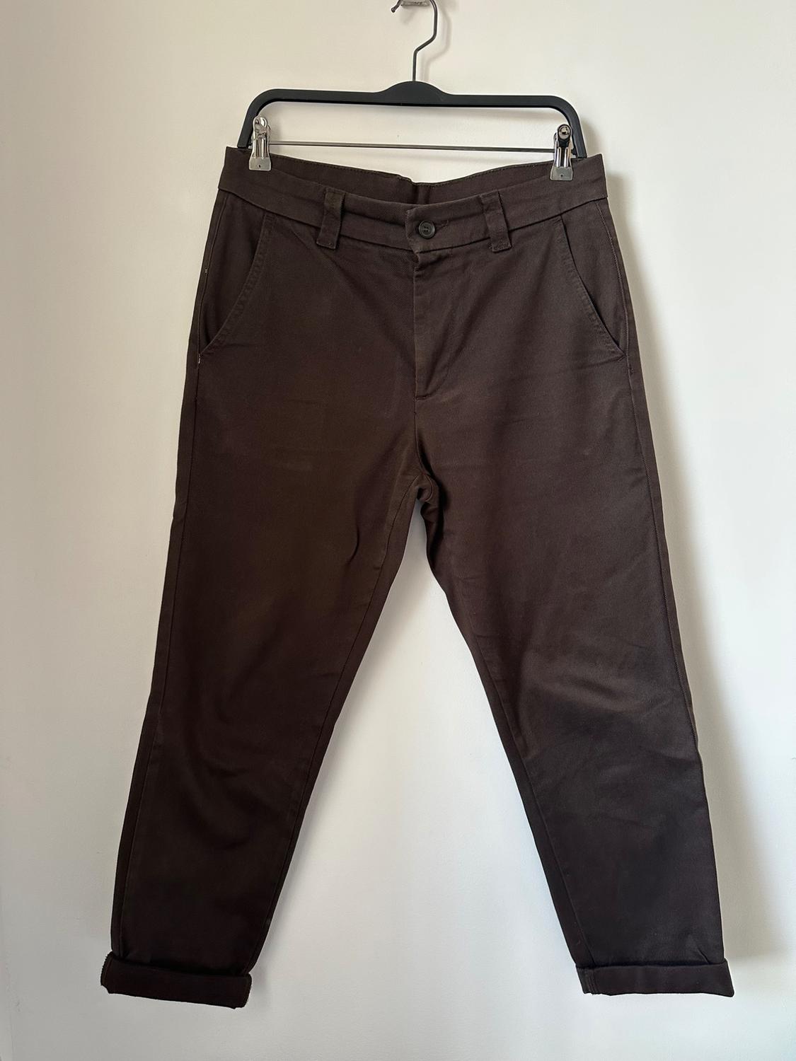 Brown trousers hanging on a black hanger against a white background. Classic design with side pockets and a rolled hem.