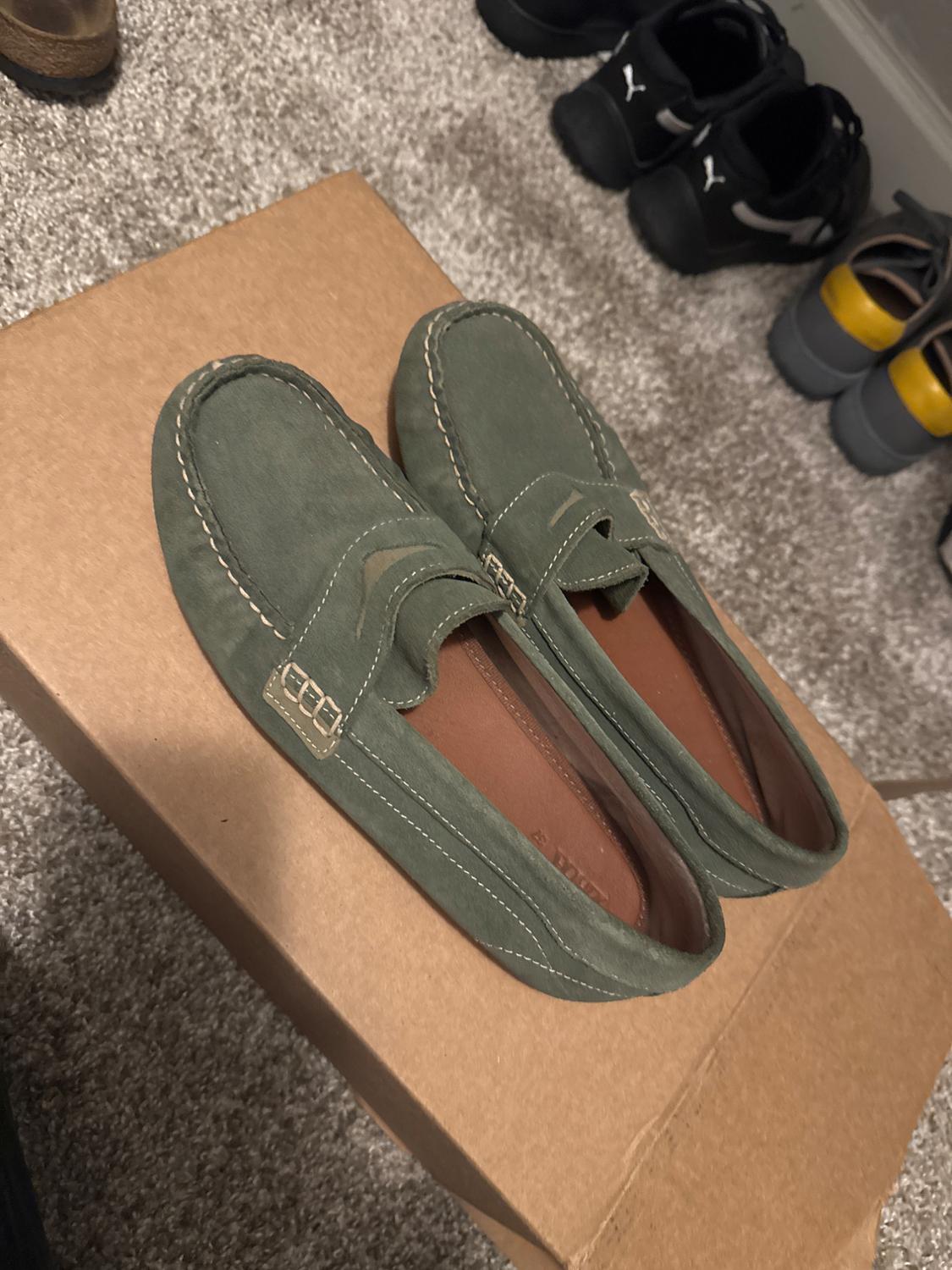 Green men's shoes on a cardboard box, with visible stitching and a classic design.