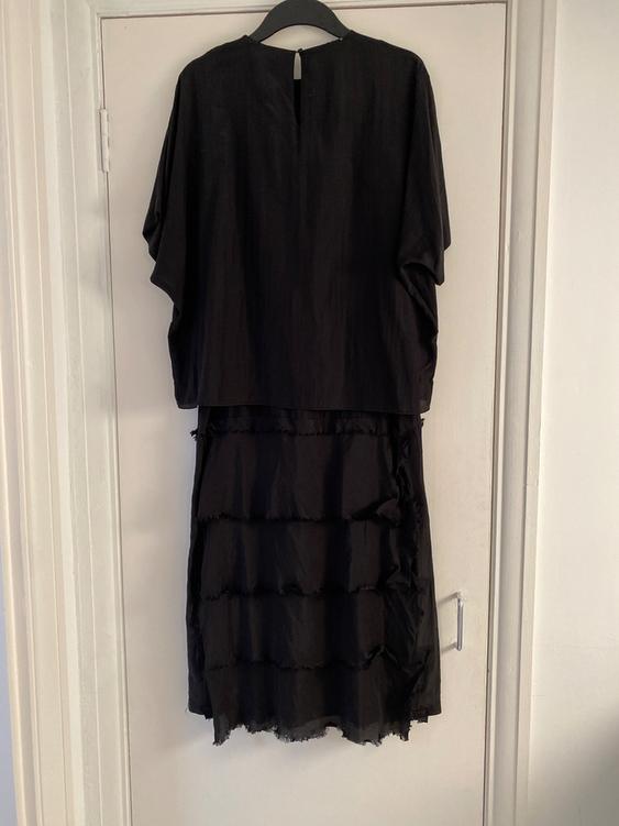 Short-sleeved black dress hanging on a white door. The skirt has layers with frayed edges.
