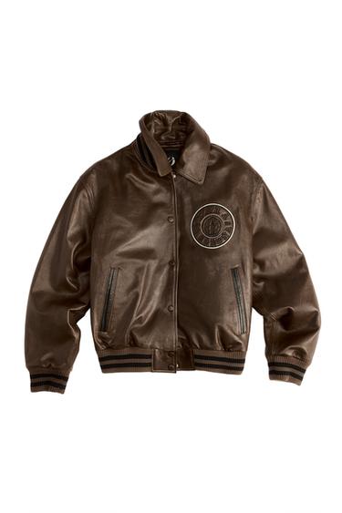 Front view of a brown jacket with a high neck, side pockets, button fastening and the text "ZARA AGRUB" on the chest.