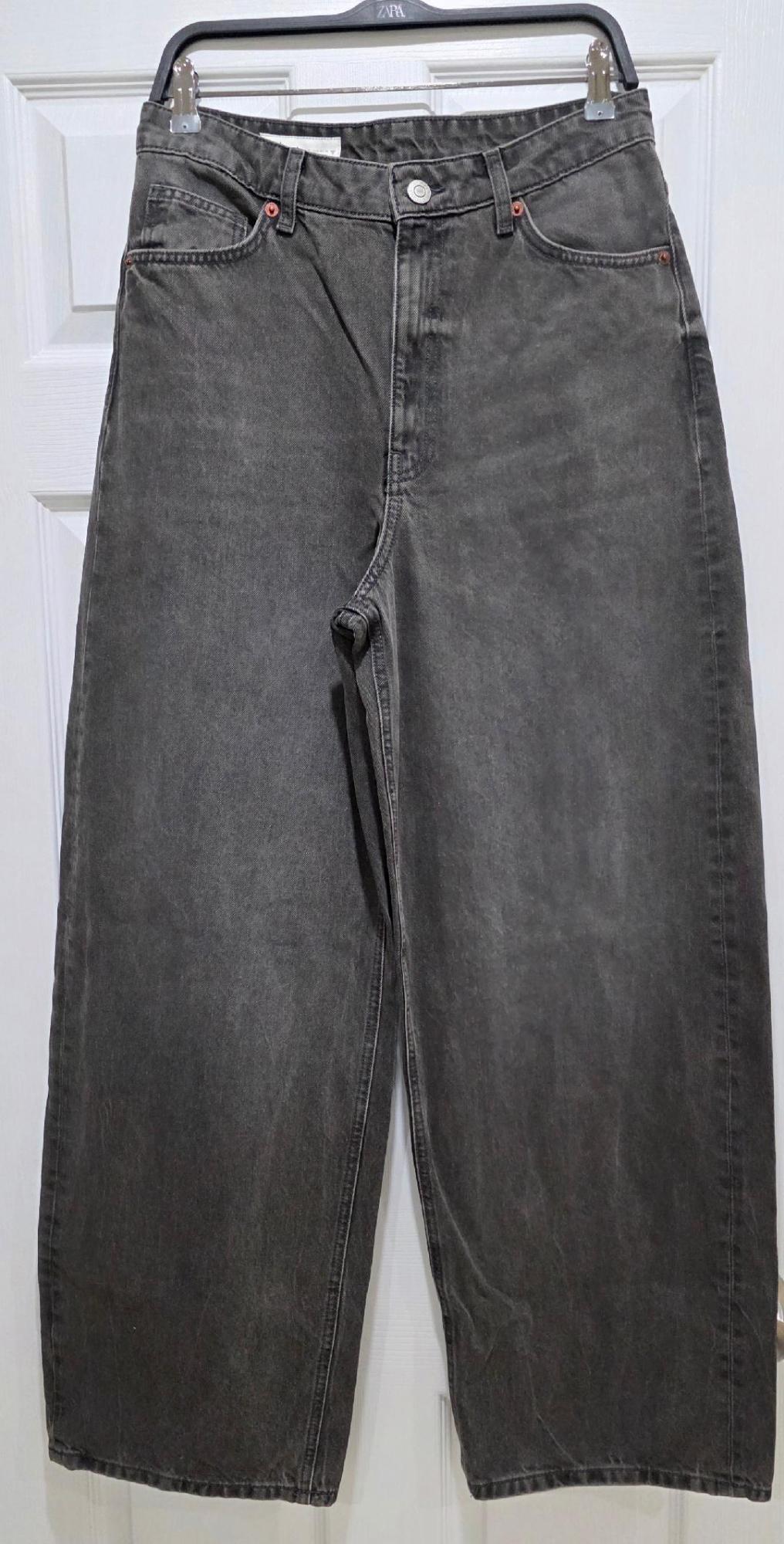 Grey jeans hanging on a black hanger in front of a white door.