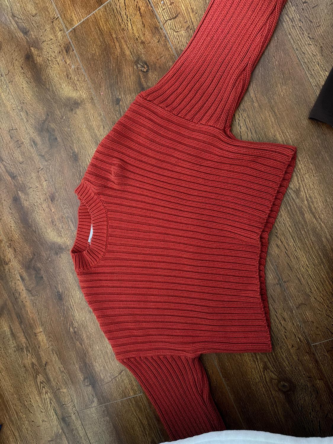 Red ribbed knit jumper spread out on a brown wooden floor.