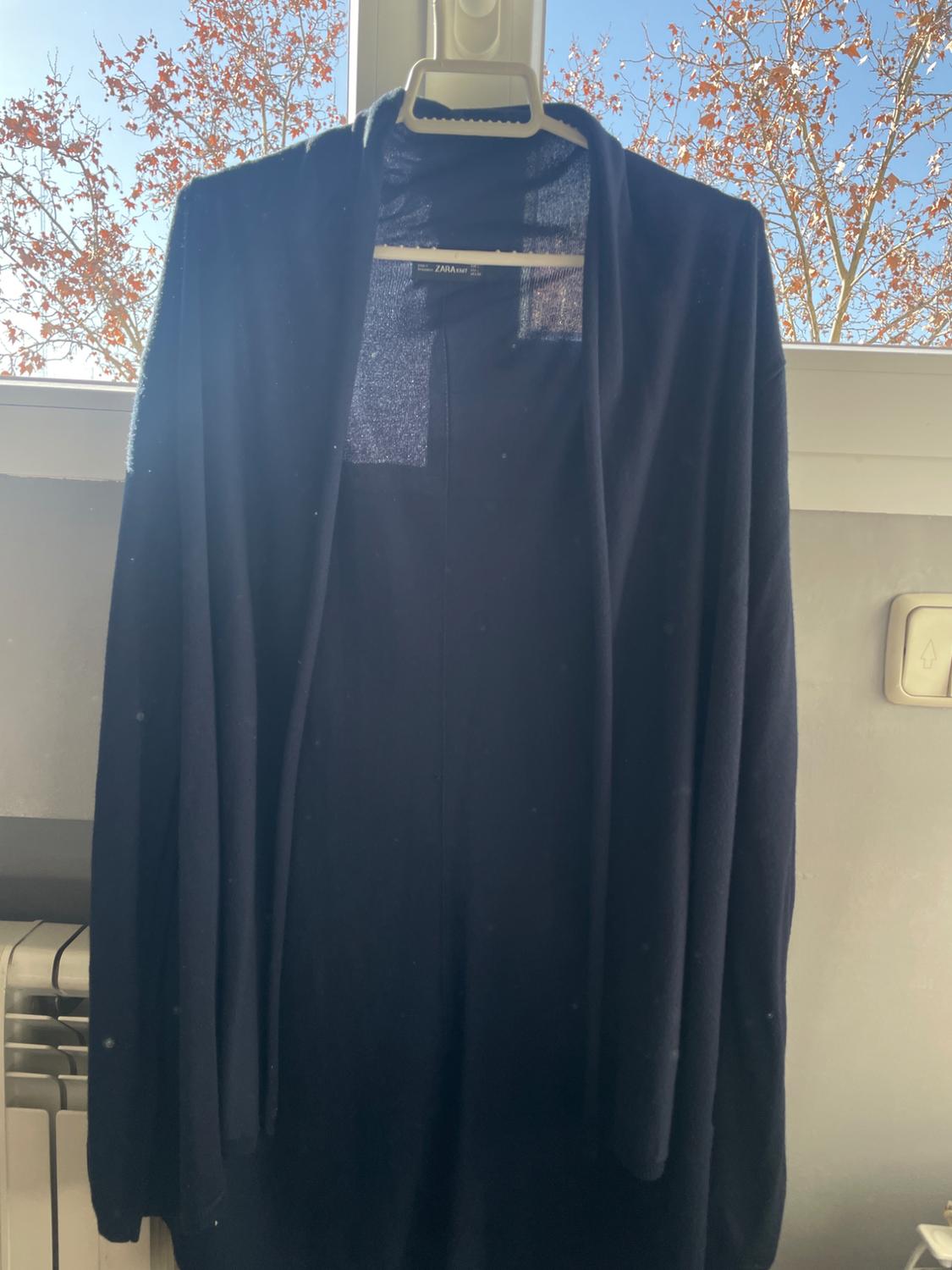Front view of a black coat hanging on a hanger, with an open collar design and no visible buttons.