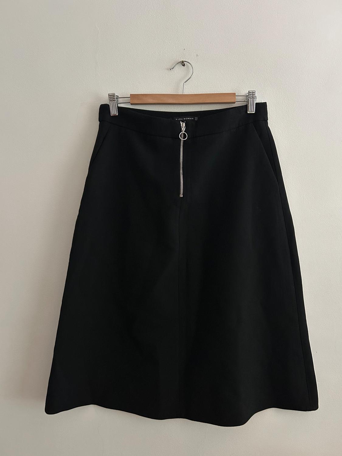 Black skirt hanging on a wooden coat hanger, with a silver front zip, against a white backdrop.