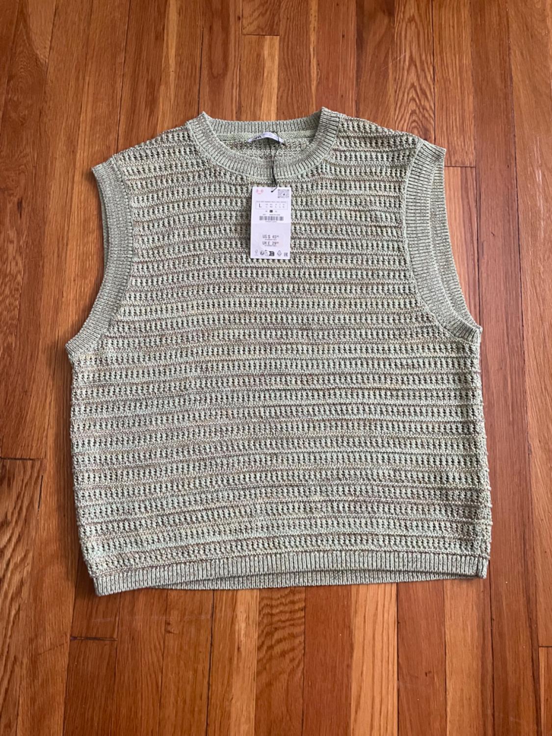 Light green open-knit waistcoat with a round neck on a wooden floor. Label with text L US $ 45 UK £ 29.