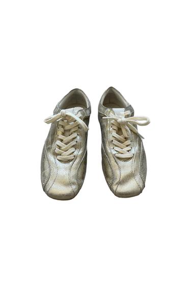 Pair of casual trainers in a metallic gold tone with white laces, photographed from above against a white background.