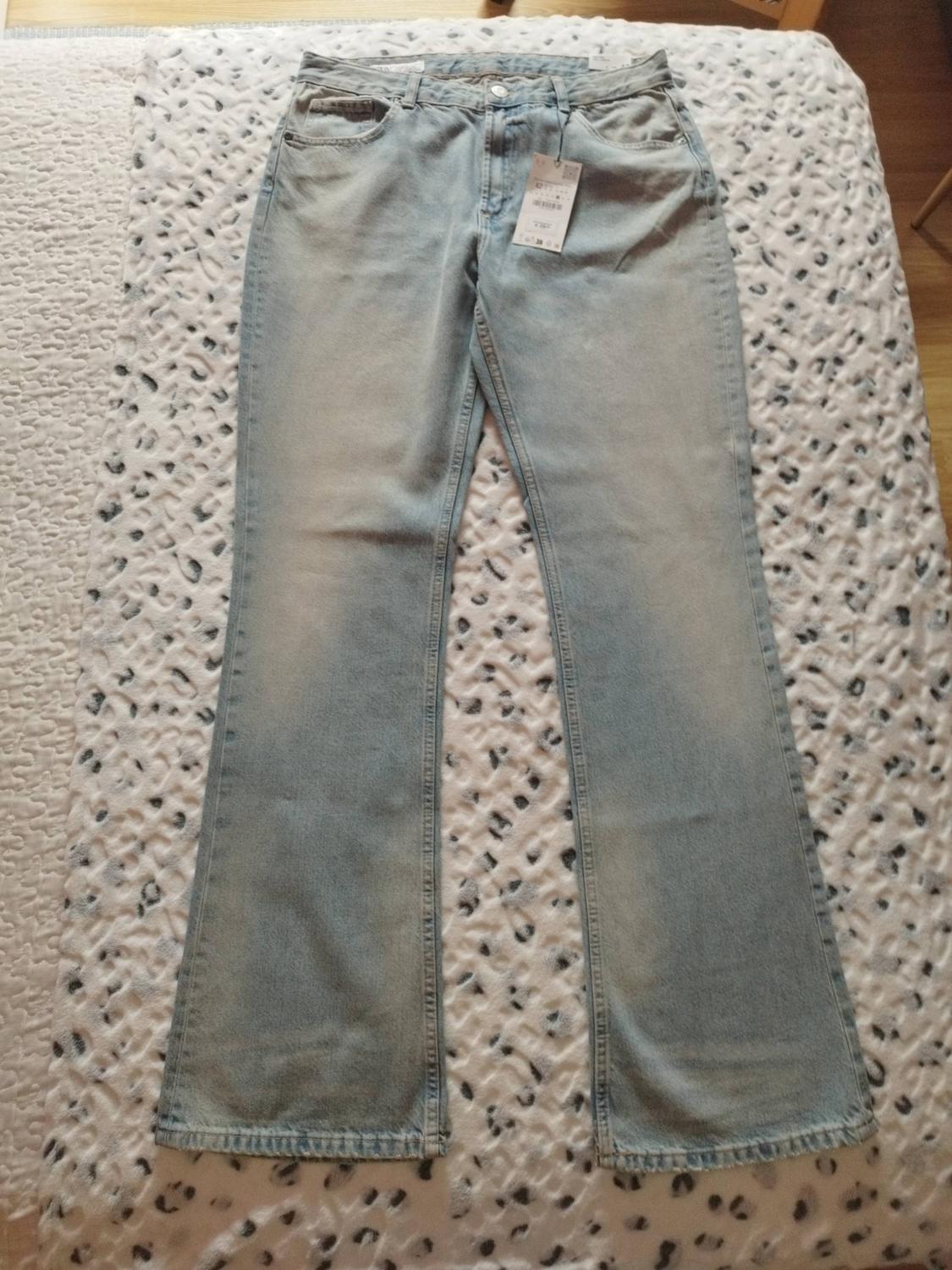 Light blue flared jeans with tags, laid out on a white blanket with a black spotted print. Casual style.