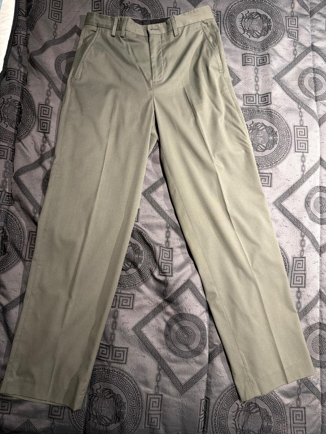 Beige trousers on a grey bedspread with geometric and circular patterns. The light highlights the fabric's weave and creases.