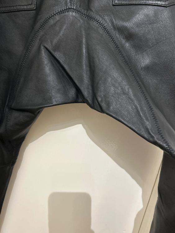 Detail of a black leather garment with visible stitching and folds, hanging against a light background.