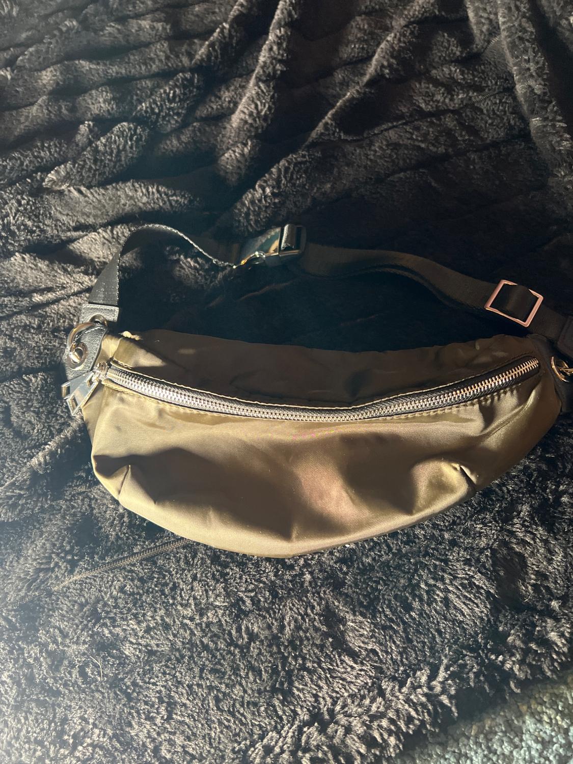 Brown fanny pack with a silver zipper on a black furry textured blanket, illuminated by soft light.