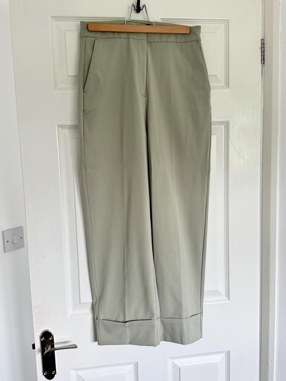 Beige trousers hanging on a wooden coat hanger over a white door. Simple design with side pockets.