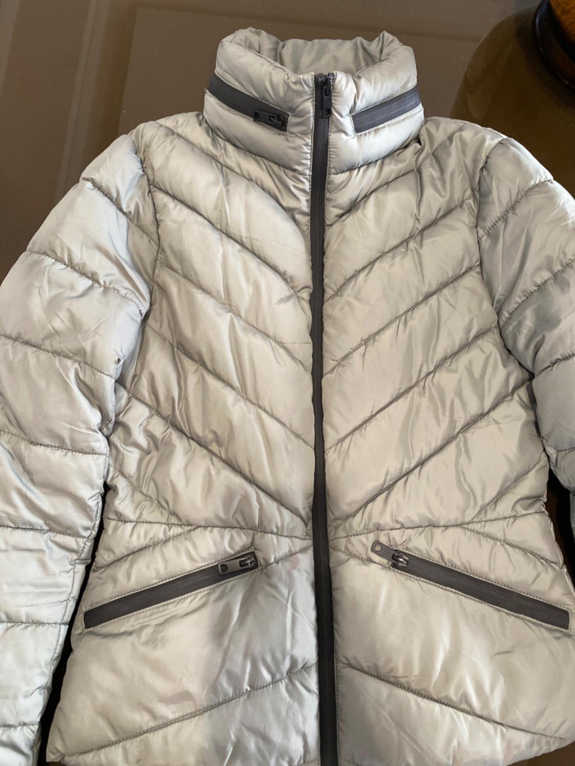 Light grey padded jacket with front zip and side pockets with fastening. Diagonal line design.