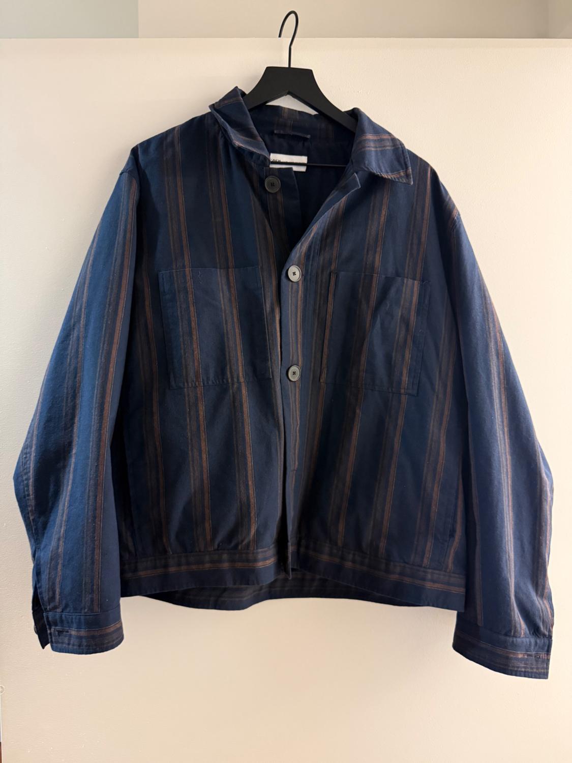 Blue and brown vertical striped jacket hanging on a black hanger against a white background.