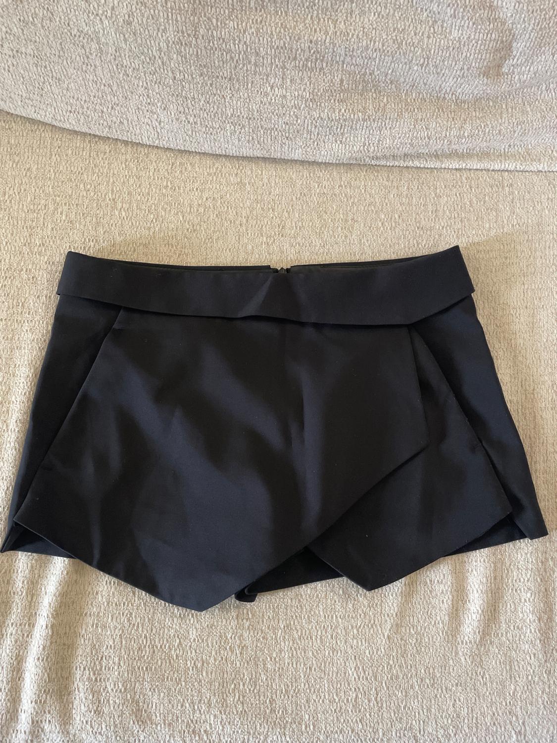Black mini skirt with an asymmetric design on a beige surface.