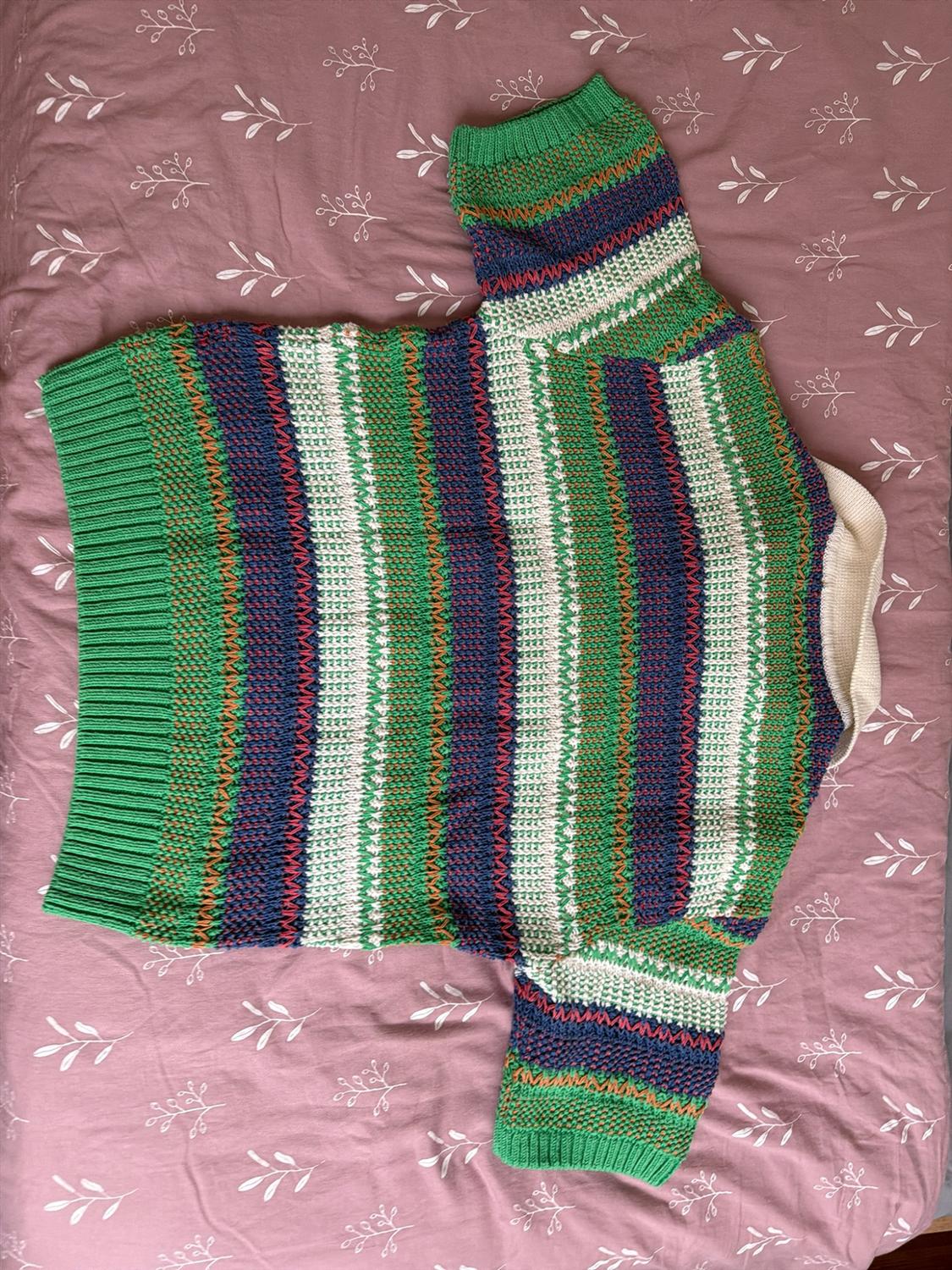 Green, white, and blue striped knit sweater with orange details,
on a pink sheet with a white leaf print.