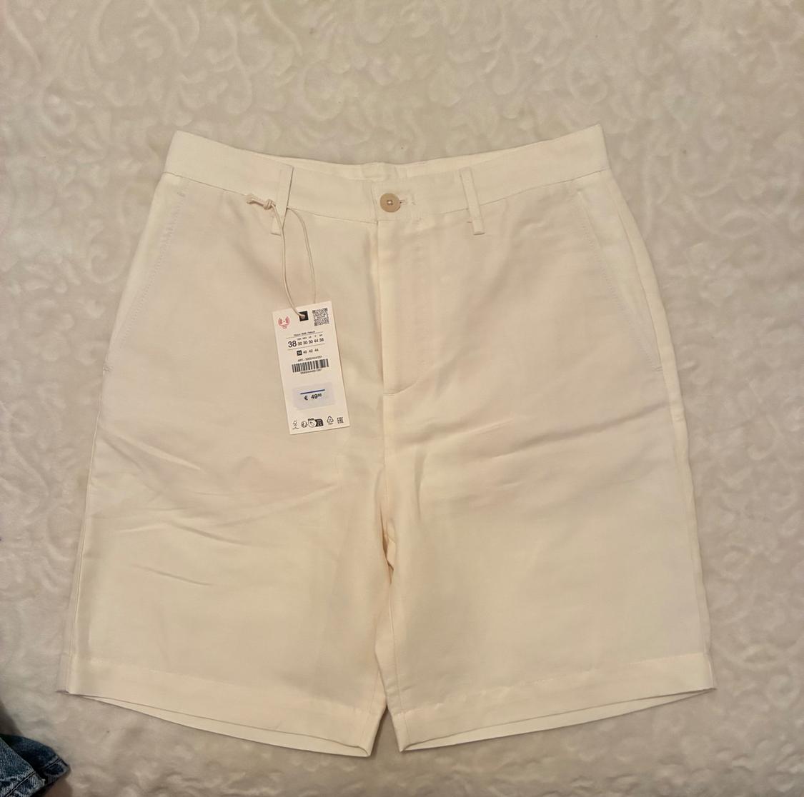 Beige shorts on a textured surface, with a hang tag showing size 38 and various symbols.