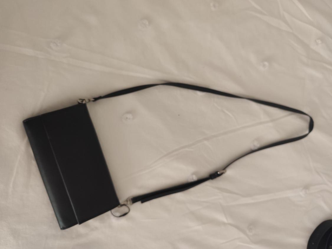 Black handbag with a long strap on a white padded surface. The image has a relaxed and minimalist style.
