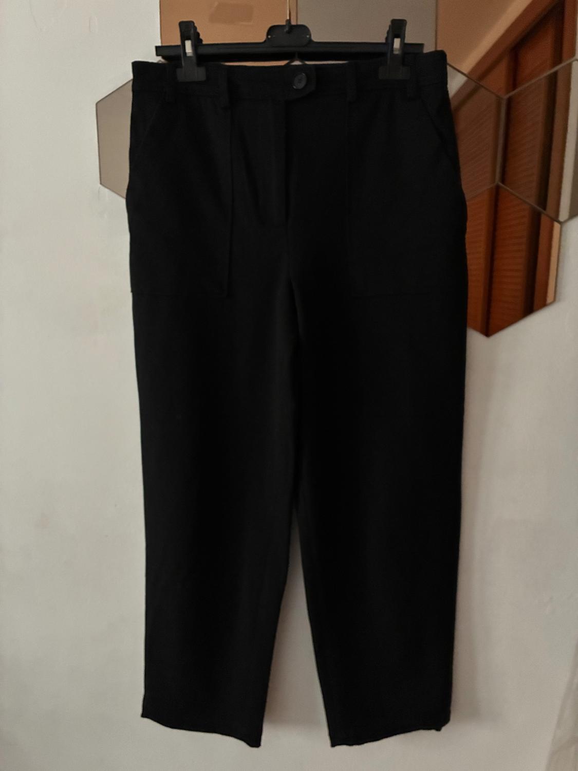 Black trousers hung on a hanger against a white background. The image shows a simple and elegant design.