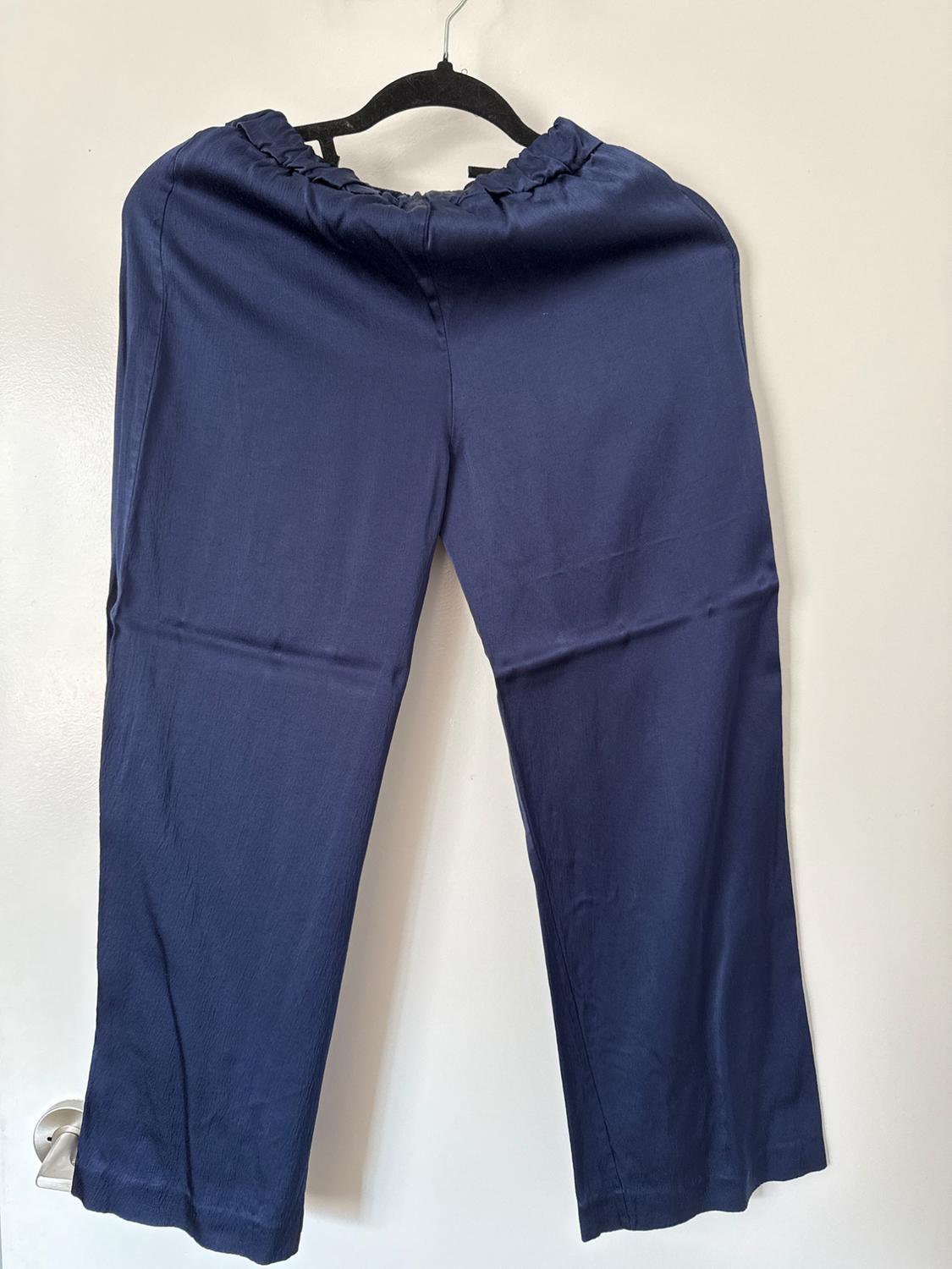 Navy blue trousers in flowing fabric with an elasticated waist, hanging on a black hanger on a white door with a silver knob.