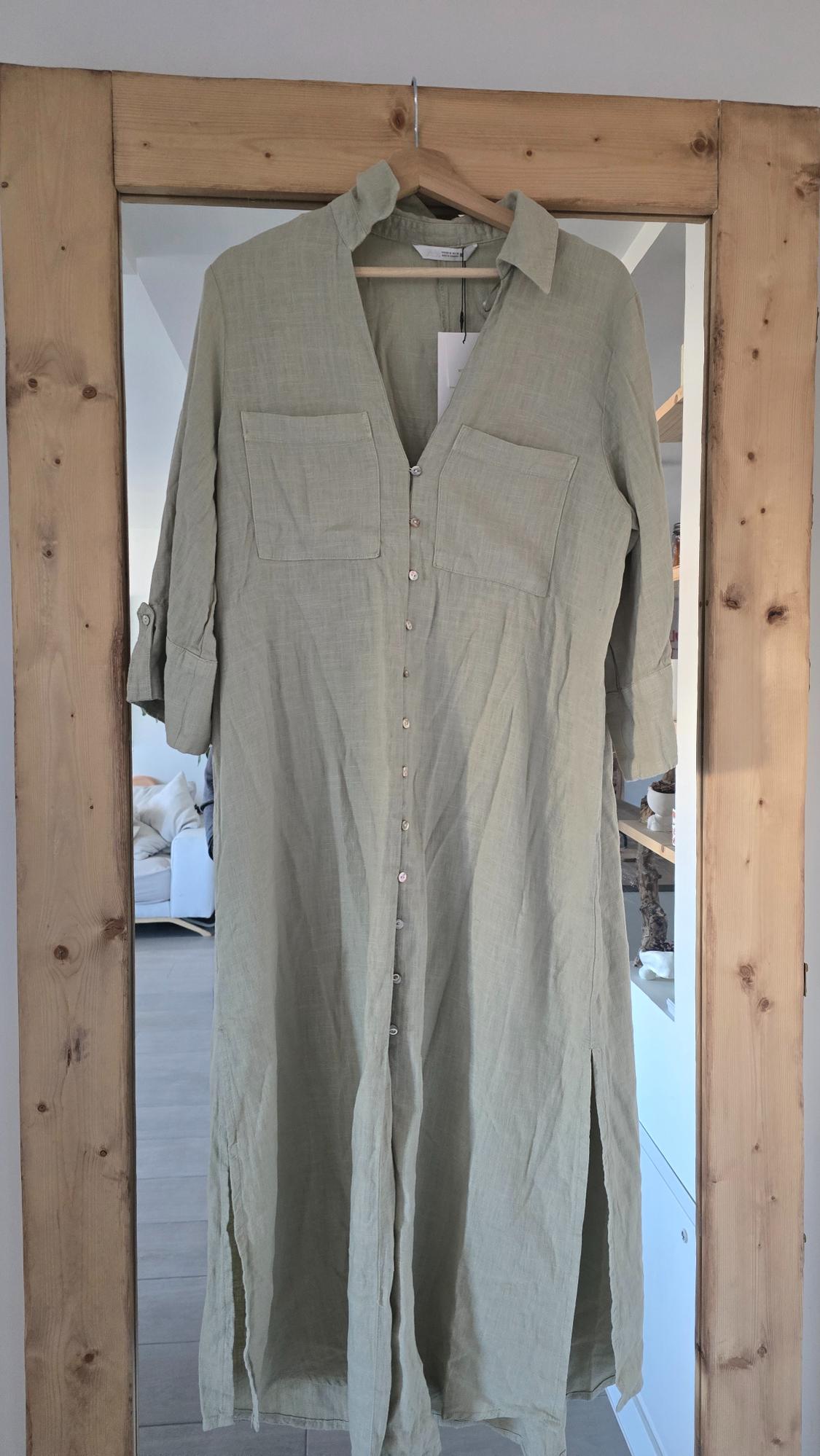 Light green linen maxi dress with front buttons and chest pockets, hanging on a wooden hanger in front of a mirror.