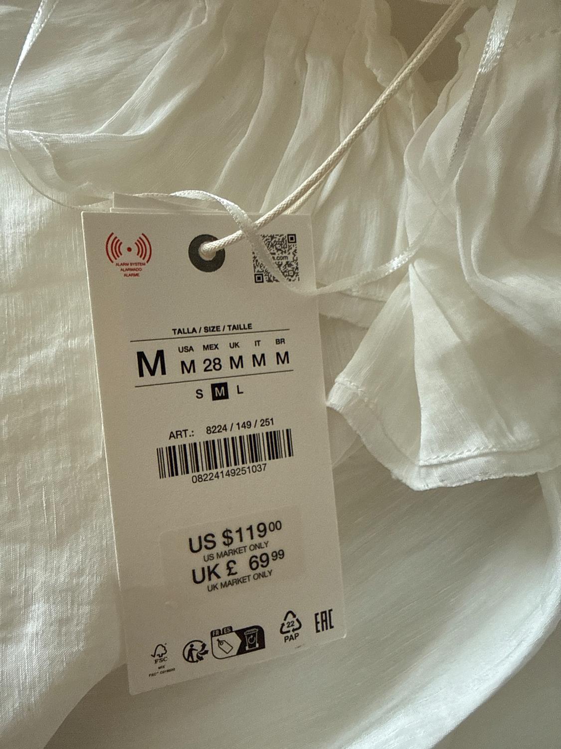 White clothing label with sizes M, prices US $119 and UK £69.99. Includes barcode and care symbols.