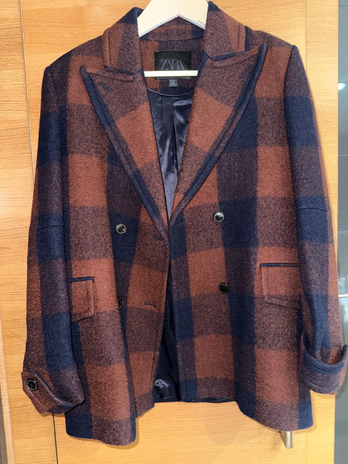 Brown and navy checked jacket hanging on a white hanger. Visible label with the text "ZARA".