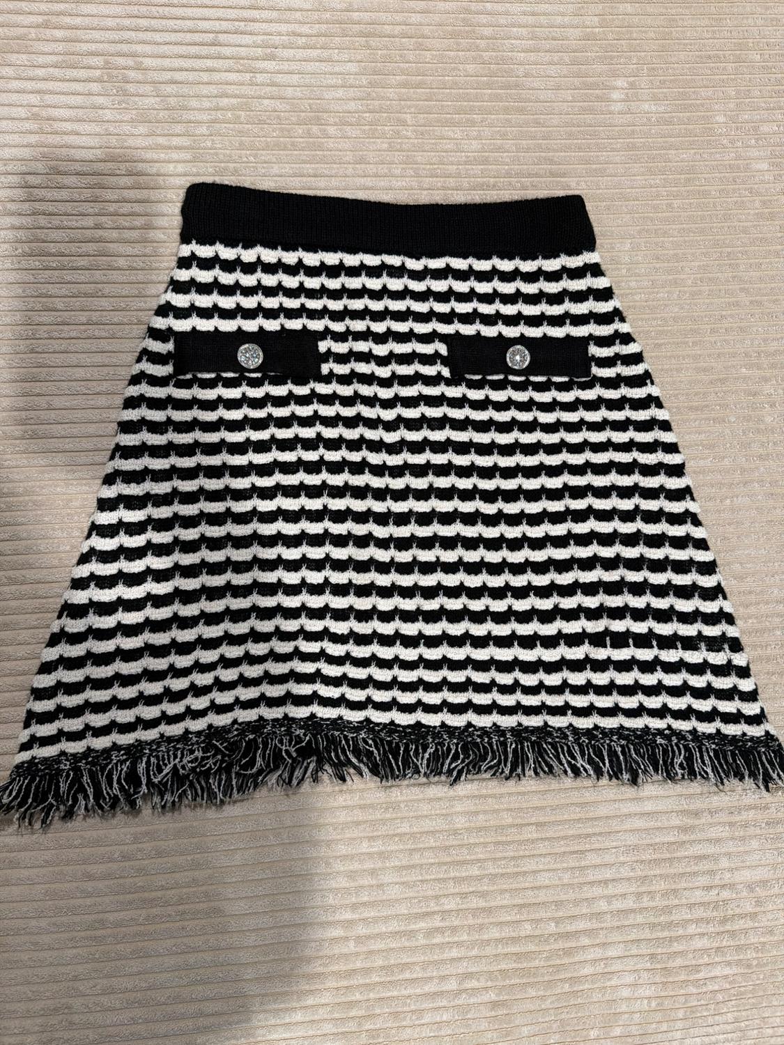 Short black-and-white striped skirt with a wavy texture, black waistband, two pockets with silver buttons, and a fringed hem.