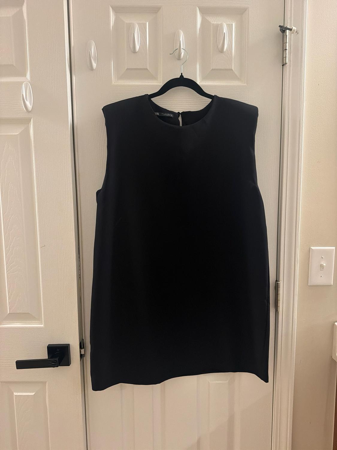 Black sleeveless dress hanging from a hanger on a white interior door. Casual and relaxed style.