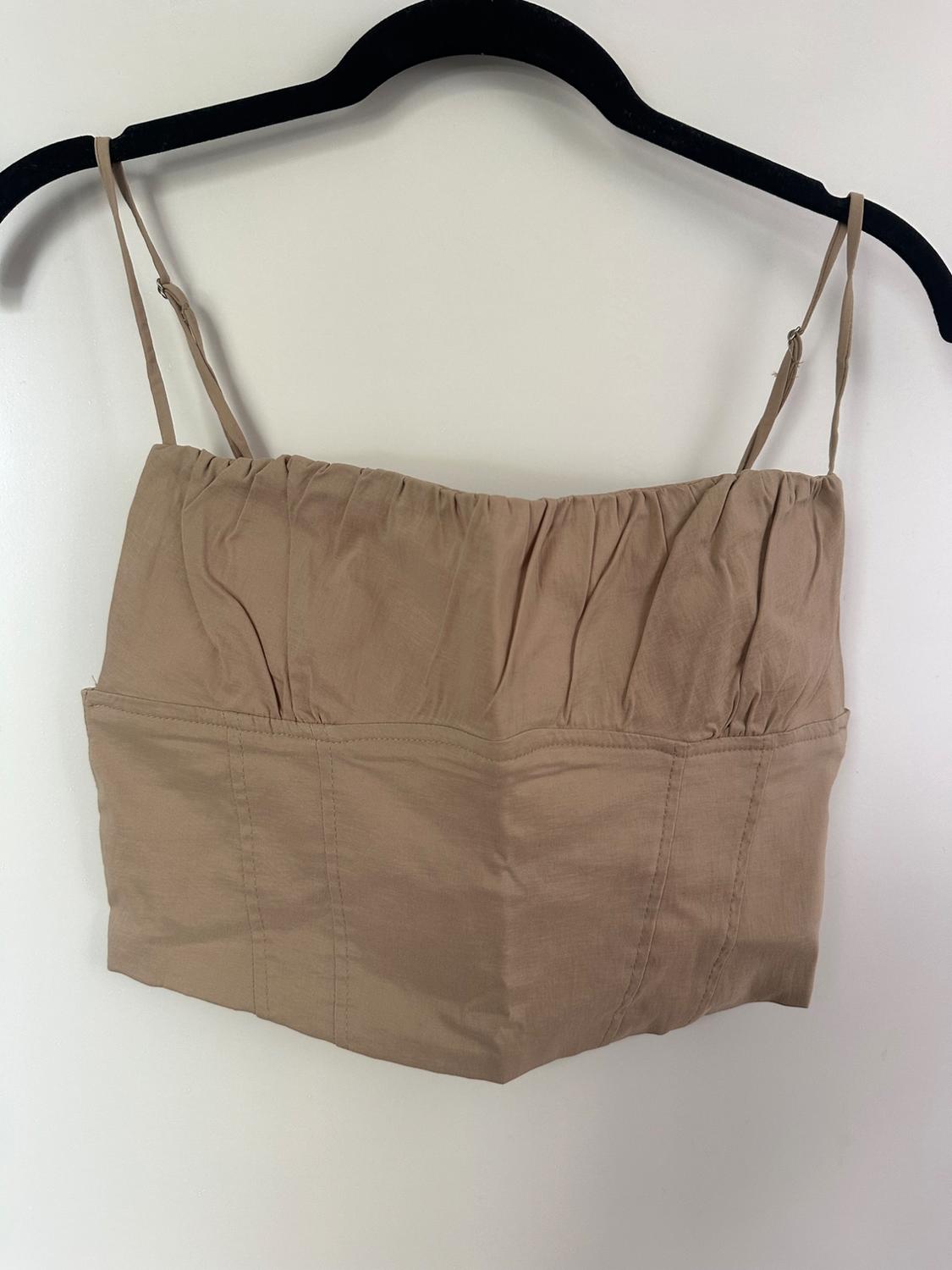 Beige corset-style crop top with spaghetti straps, ruched bust, and vertical seams, hanging on a black hanger against a white background.