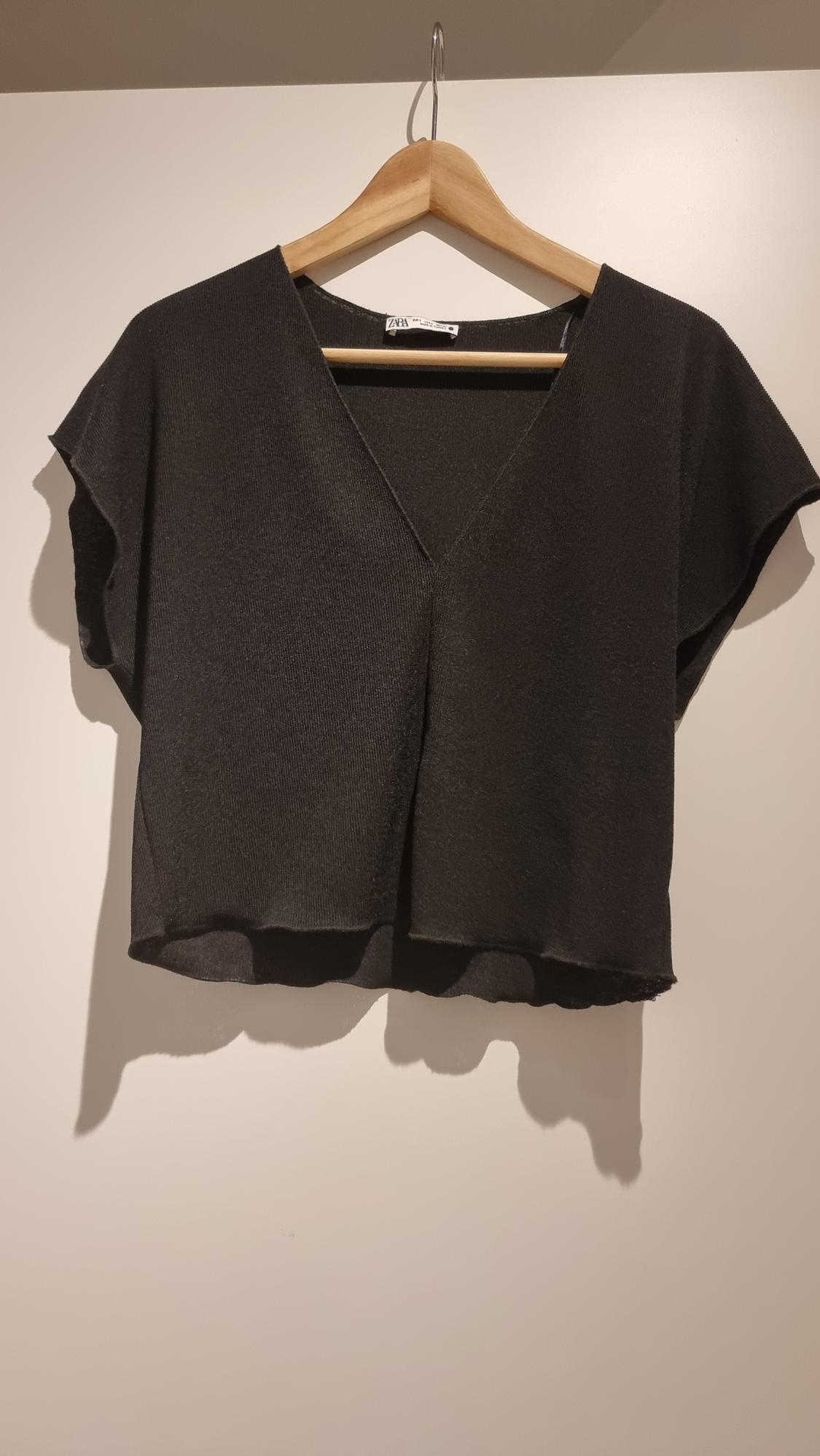 Black short-sleeved V-neck blouse hanging on a wooden hanger against a white background.