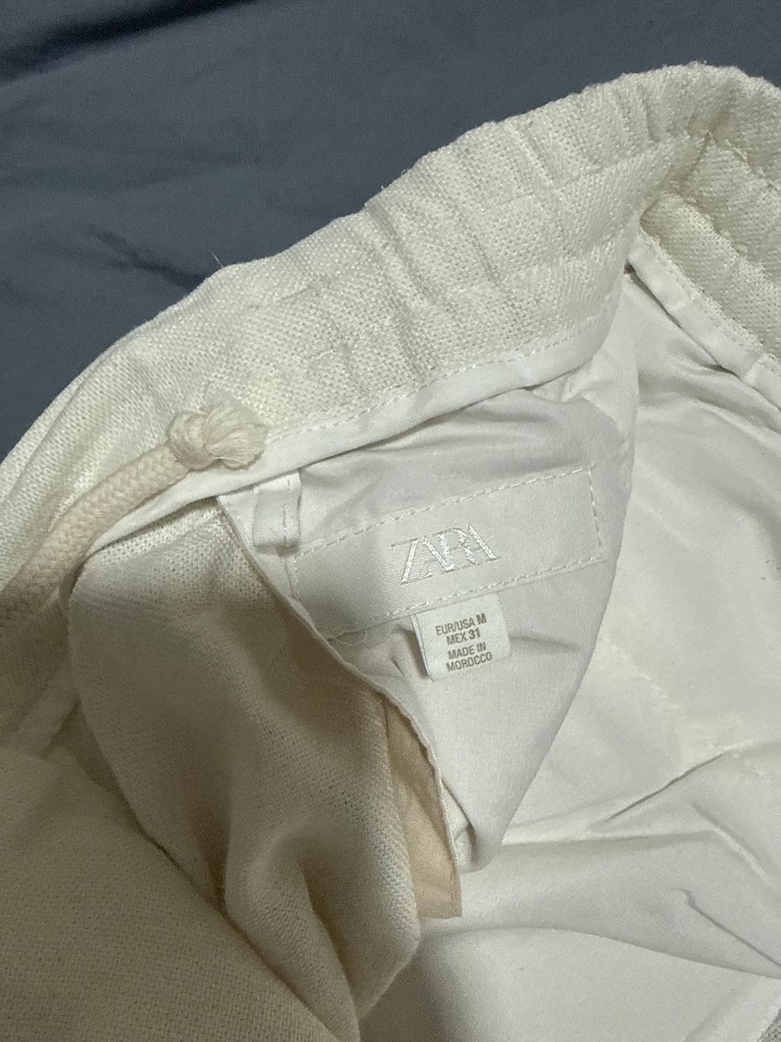 White inner clothing label with the brand "ZARA" and size "EUR/USA M, MEX 31, MADE IN MOROCCO" on a grey fabric background.
