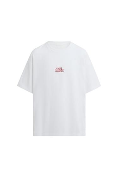 White T-shirt with red text "CAFFÈ D'AUTORE 2023 MILANO ITALIA" in the centre. White background.