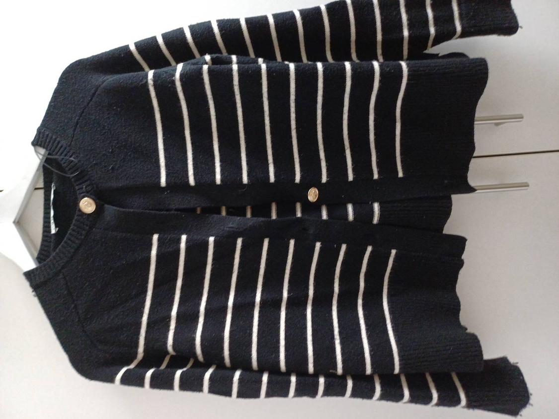 Black knitted cardigan with horizontal white stripes and gold buttons, hanging on a white hanger against a light background.