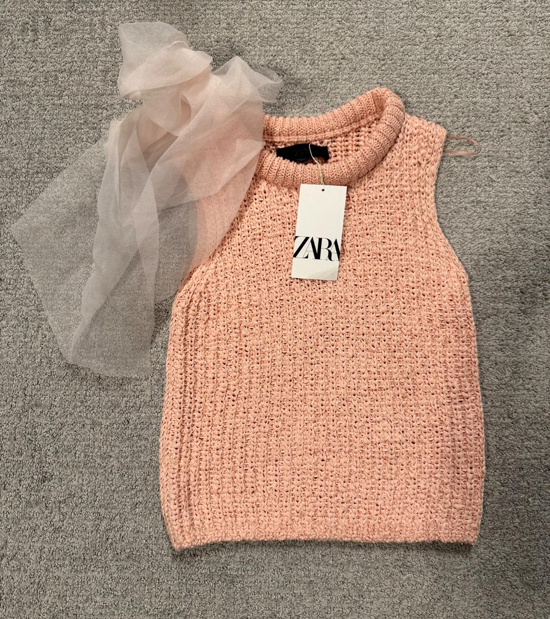 Pink knit top with a high neck and Zara tag on a gray rug. Light pink tulle fabric on the left side.