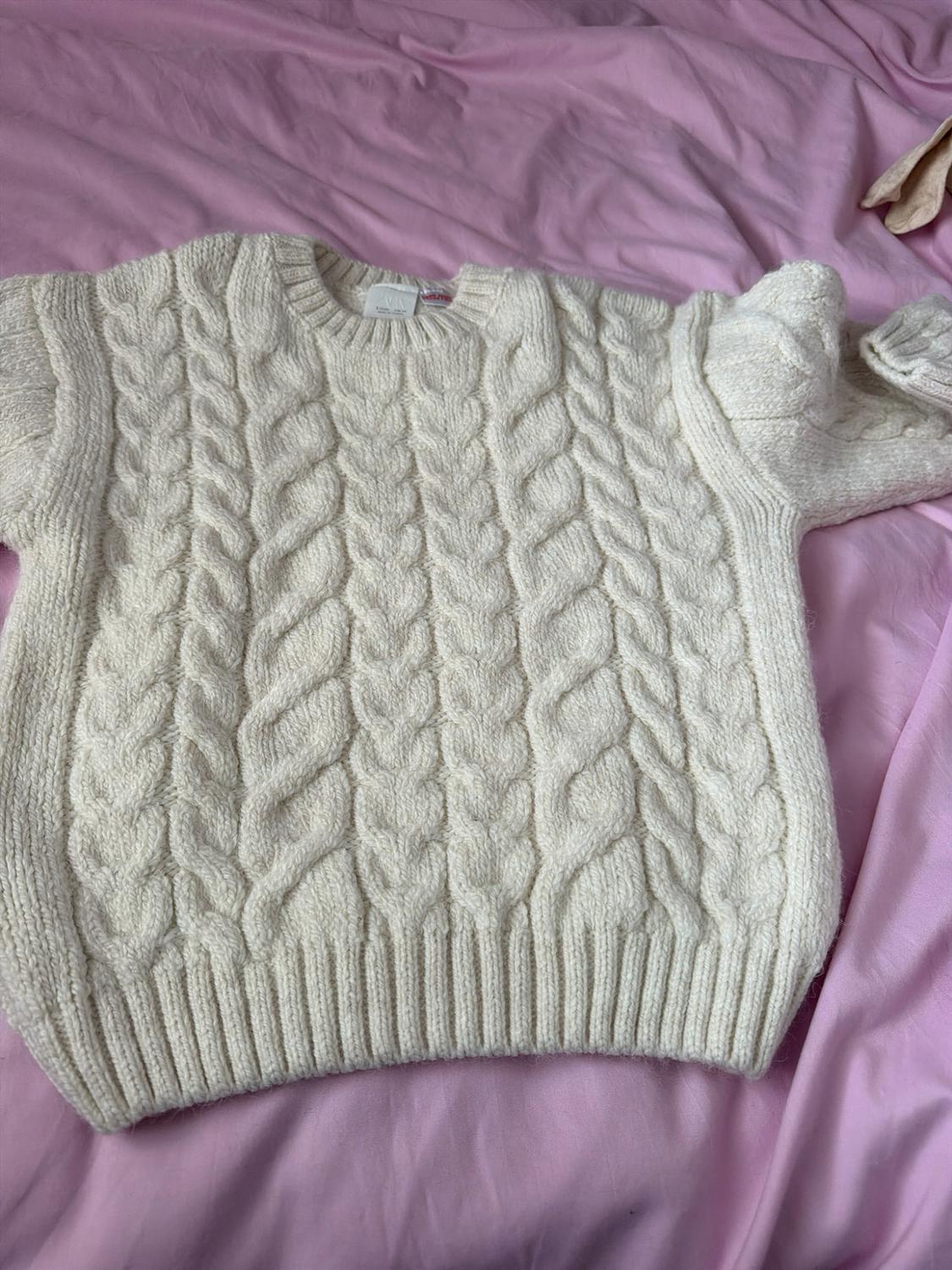 Chunky cable-knit jumper in ecru, laid on a crinkled pink fabric.