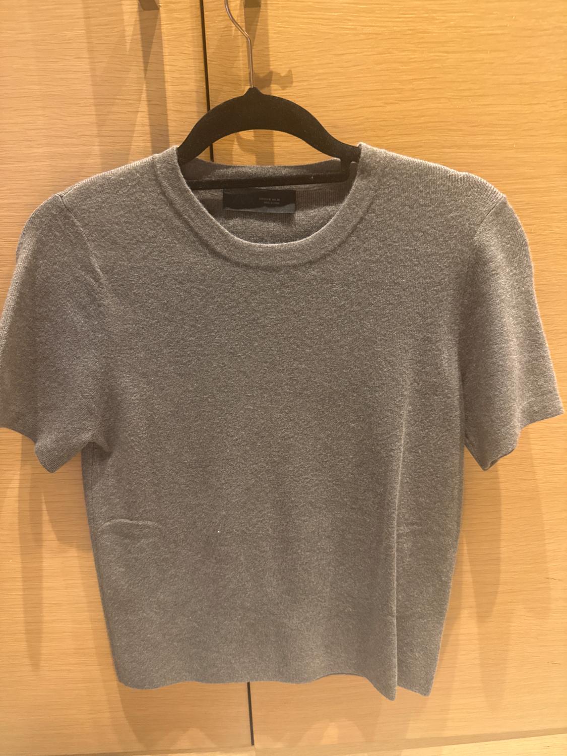 Grey short-sleeved t-shirt hanging on a black hanger against a light wood background.