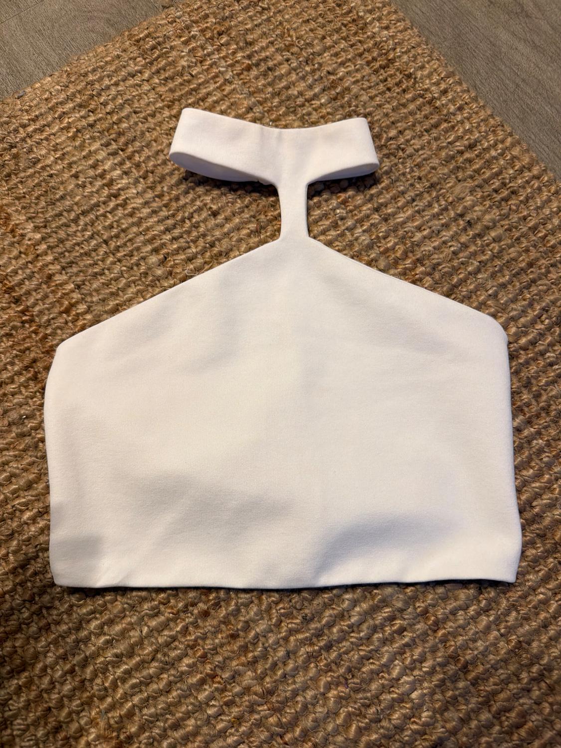 White crop top with a high neck and a chest cutout, placed on a rustic brown woven rug.