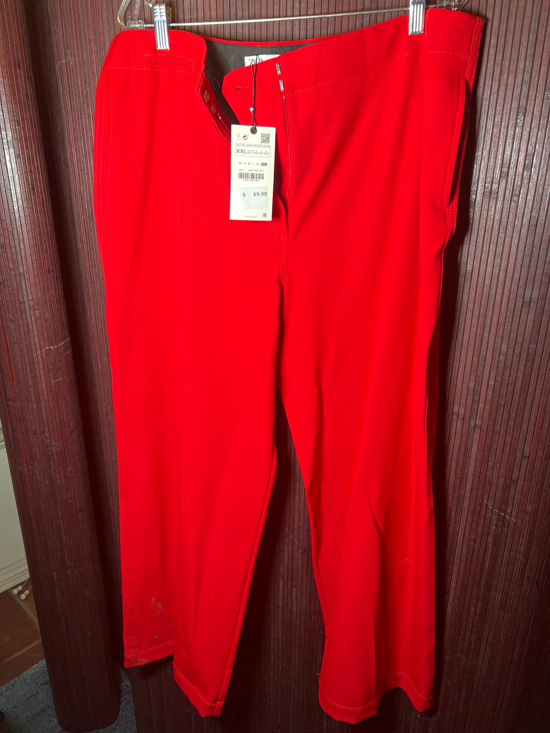 Red pants hanging on a hanger with a visible tag showing the price of $69.90, against a brown wooden background.