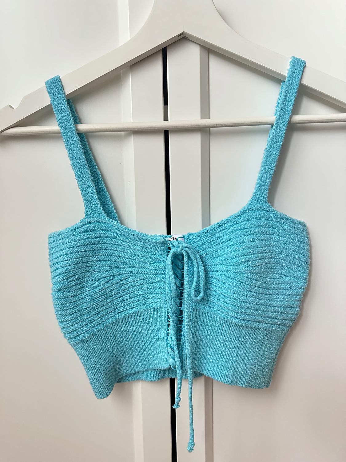 Light blue knitted crop top with straps and adjustable drawstring front, hanging on a white hanger.